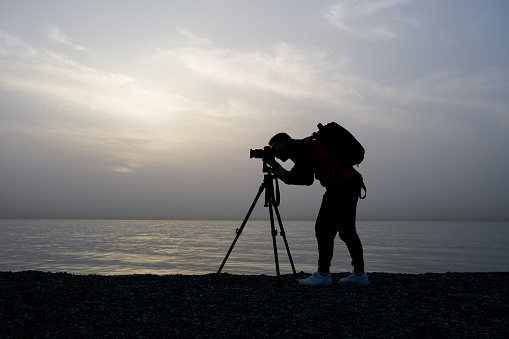 A young man takes a photo on the beach at sunset.