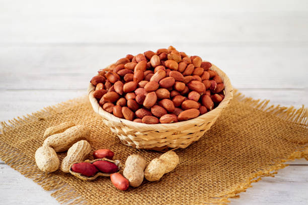 istock Peanuts Heap in a Wicker Basket on a Table Covered with Burlap in a Light Background. Roasted Arachis Nuts Pile, Heap of Peanut, Whole Groundnut with Shell, Macro Peanut Side View on White Background 2150028295