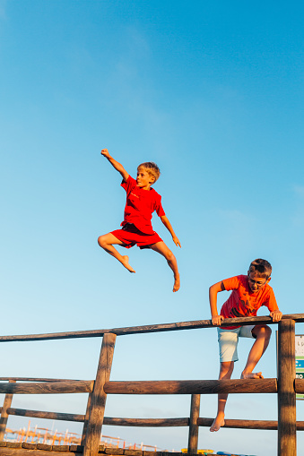 Group of children enjoys summer vacation and having fun jumping from a pier’s fence on the beach