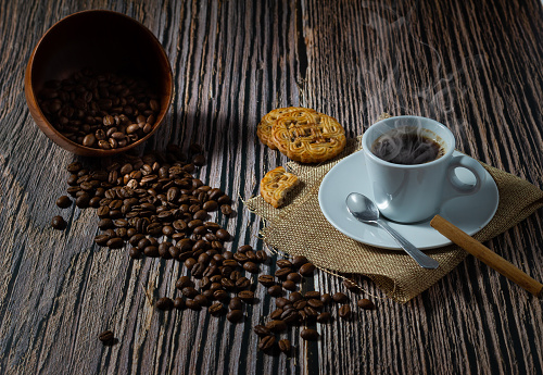 Cup of hot coffee , homemade cookie, cinnamon and coffee beans on wooden background.