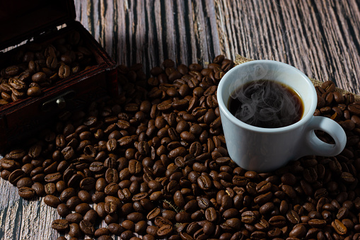 A cup of coffee between selected roasted coffee beans on wooden background.