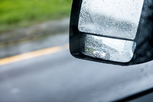 The rear view mirror of the car is covered in drops of rain.