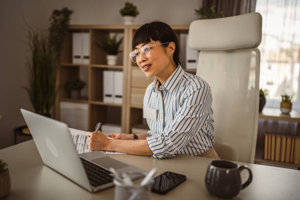 istock Mature japanese woman with eyeglasses hold pencil and write on document 2150039416