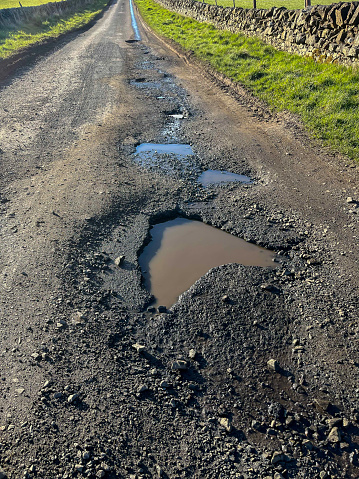 A rural lane, destroyed by potholes, which are making it dangerous and difficult for drivers and cyclists trying to travel in the Scottish Borders. The holes are being flooded by run off water where ditches are blocked. Local authorities are struggling to carry out repairs, with so many roads damaged and in need of urgent repairs.