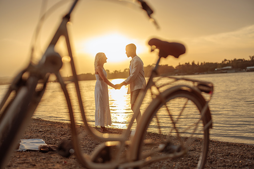 Shot of a sunset by the river and a lovely couple while they are holding hands and looking at each other