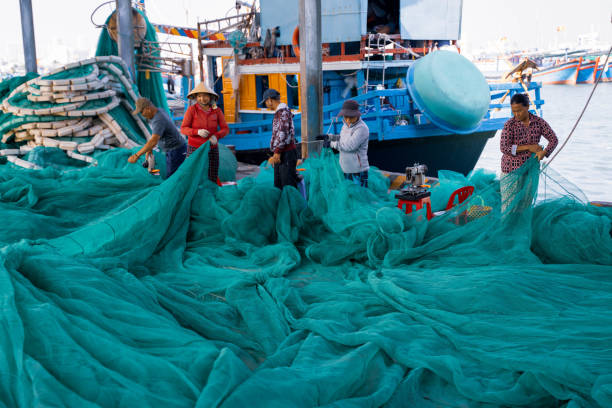 Ho Chi Minh, Vietnam - 4 March 2024 : At the pier in Ho Chi Minh City, Vietnam, men and women are weaving a beautiful turquoise fishing net in preparation for the next fishing trip