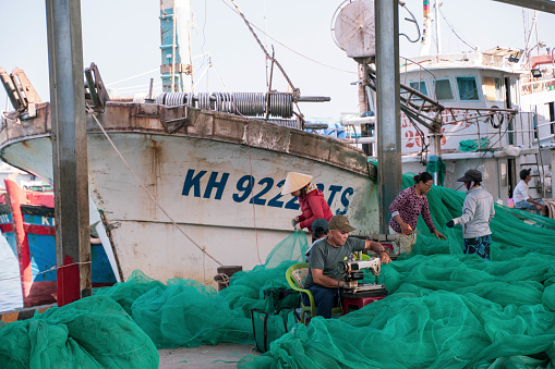 Ho Chi Minh, Vietnam - 4 March 2024 : At the pier in Ho Chi Minh City, Vietnam, men and women are weaving a beautiful turquoise fishing net in preparation for the next fishing trip