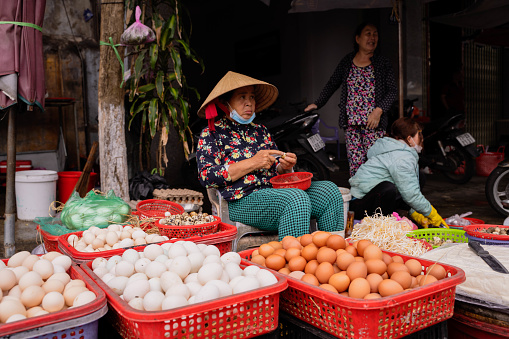 Ho Chi Minh, Vietnam - 4 March 2024 : An old woman selling vegetables at a street market in Ho Chi Minh City. Her traditional hats can be seen across Vietnam