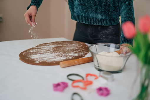 Image of a woman's hands sprinkling flour onto dough and making cookies for the holidays.