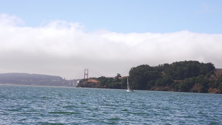 Sailing down the San Francisco bay on a small yacht in California near a Golden Gate bridge and Alcatraz prison island and San Francisco downtown on the horizon.