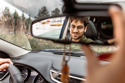 Young man with eyeglasses driving a car, reflection in rear mirror