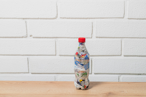 one eco brick PET bottle stuffed with plastic waste with white brick wall background and space for text and copy