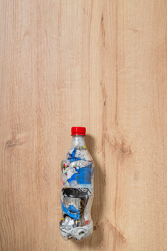 Small PET plastic bottle filled with plastic waste to serve as an eco brick over wood background with space for text and copy
