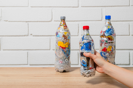 Three bottles of eco brick PET bottle stuffed with plastic waste and one is holded by  a hand, with a white brick wall background