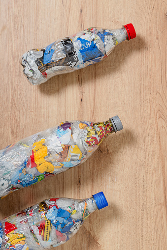 Three bottles of PET that are filled with plastic waste to serve as eco bricks, organized arranged diagonally over wooden background