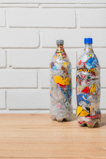 two PET bottles filled with plastic waste for eco bricking on wood surface and wite brick background with space for text and copy