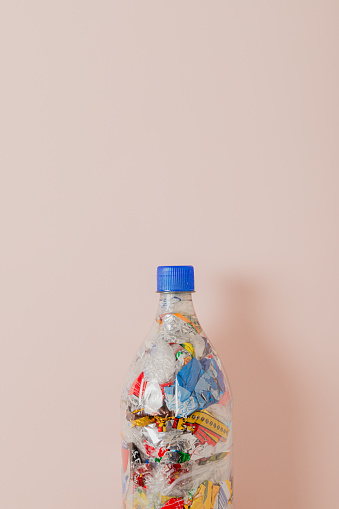 top part of eco brick PET bottle stuffed with plastic waste on light pinck background and empty space for text and copy
