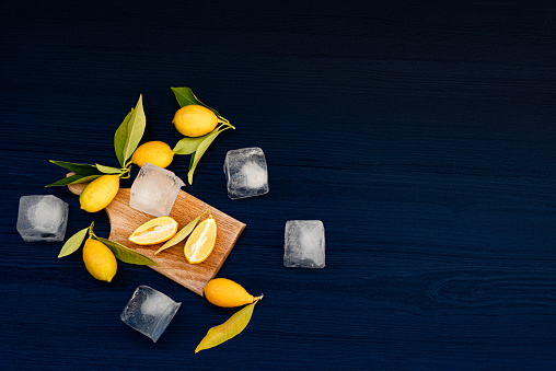 Fresh Lemons with Leaves and Ice Cubes on Dark Blue Wooden Background