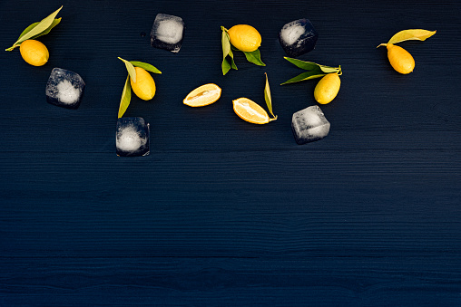 Fresh Lemons with Leaves and Ice Cubes on Dark Blue Wooden Background
