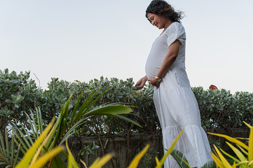 A glowing pregnant woman enjoys a moment with nature, surrounded by the lakeside's lush green and yellow foliage.
