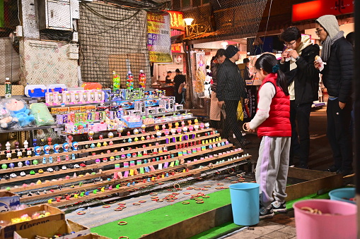 Taiwan - Jan 23, 2024: A girl tries her luck at a ring toss game in Taiwan. Ring toss is a popular game of chance at Taiwanese night markets, where players try to win prizes by tossing rings over pegs