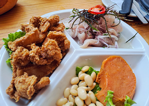 Ceviche, chicharrón de pescado y frijoles con camote, en un plato dividido en 3, sobre una mesa de restaurante.
