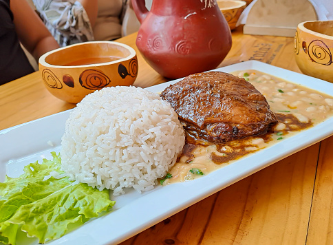 Baked hen, served with beans and rice, on a rectangular plate. Peruvian food. Gallina al horno, servida con frejoles y arroz, en un plato rectangular. Restaurante de comida peruana,