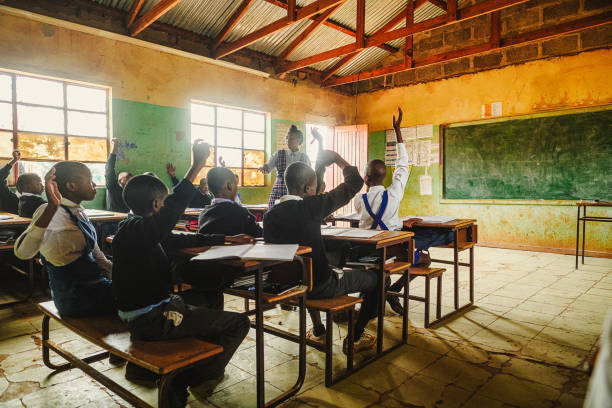 Female Teacher teaching a class of high school students in uniform in a rural school in Africa  Malealea, Lesotho.  Rear view of the learners with their hands raised.