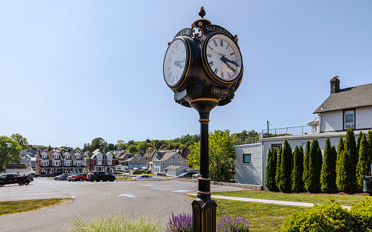 Restored street clock stands at street intersection in Nazareth, Pennsylvania. The background displays row houses with clear blue skies