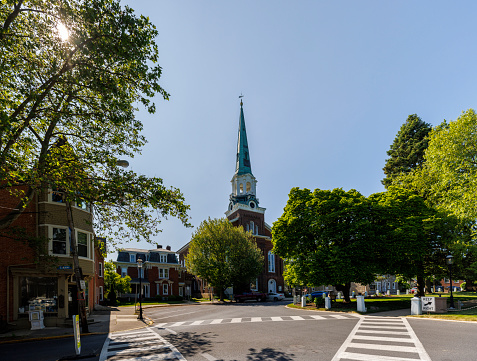 Sunny day illuminates the historic Moravian Church in Nazareth, Pennsylvania. The church, with its prominent green spire, stands as a pivotal landmark in the town, framed by lush green trees and set against a vivid blue sky. The foreground showcases pedestrian crossing