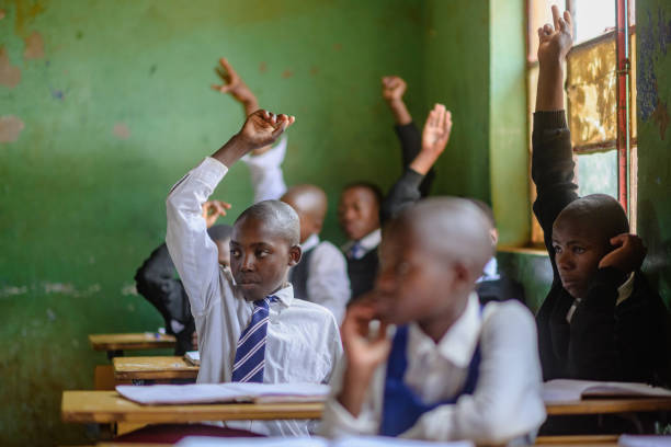istock Group of African learners wearing school uniform with their hands raised in a classroom 2150077828