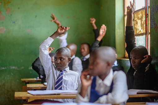 Group of African learners wearing school uniform with their hands raised in a classroom Malealea Lesotho