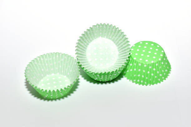 On a white background, molds made of green paper for baking cupcakes lie chaotically.