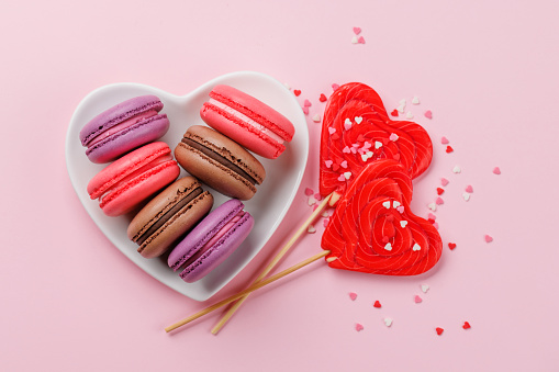 Various colorful macaroons in heart shaped bowl. Love sweets over pink background
