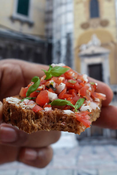 Stock photo showing close-up view of bruschetta recipe open sandwich with toasted, wholemeal bread slice rubbed with a garlic clove and topped with diced tomatoes, buffalo mozzarella cheese shavings, drizzled with balsamic vinegar, extra virgin olive oil and garnished with basil leaves.