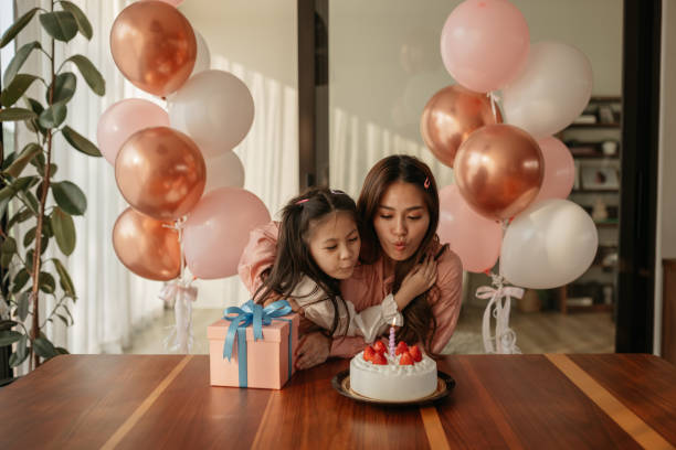 Mid-adult woman and her daughter are blowing birthday candles together.