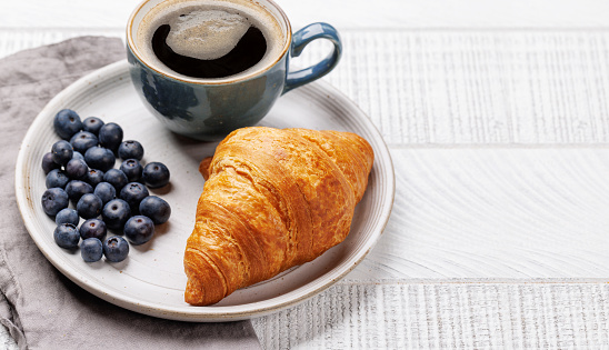 Cappuccino coffee and fresh croissant on wooden table. With copy space