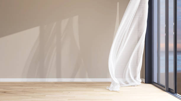 istock Empty room with large blank beige brown wall, white blowing sheer curtain, wood laminate parquet floor in evening sunlight from glass sliding door for 2150083567