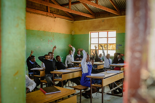 Outside view into African Secondary education in rural setting.  The pupils learners students have their hands raised.  They look keen to learn and answer questions.  Malealea Lesotho