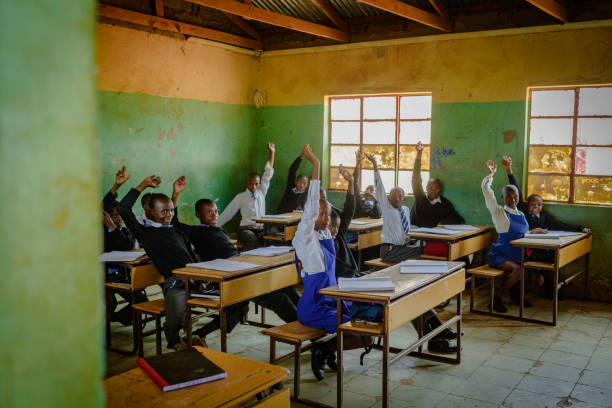 istock Outside view into African Secondary education in rural setting whole class hands raised 2150086086