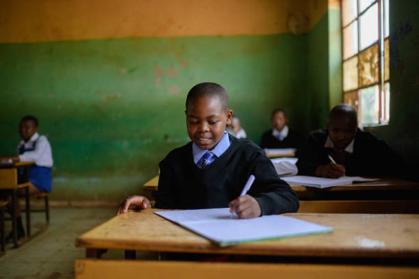 istock Cute Schoolboy in uniform sitting in classroom wrinting 2150086507