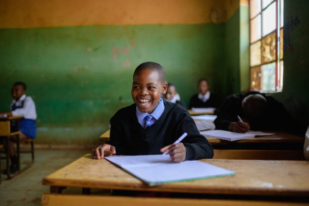 istock Cute Schoolboy in uniform sitting in classroom laughing 2150086546