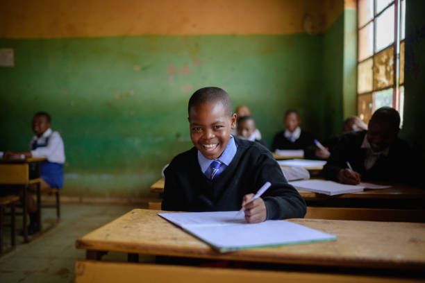 istock Cute Schoolboy in uniform sitting in classroom looking at camera laughing 2150086647