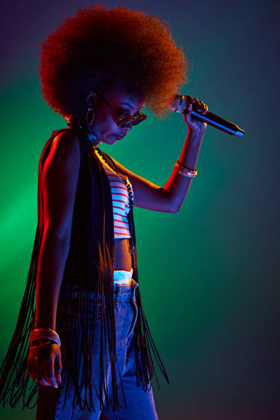 istock Afro-haired woman, talented vocalist in bohemian style performs in neon light against gradient background. 2150086672