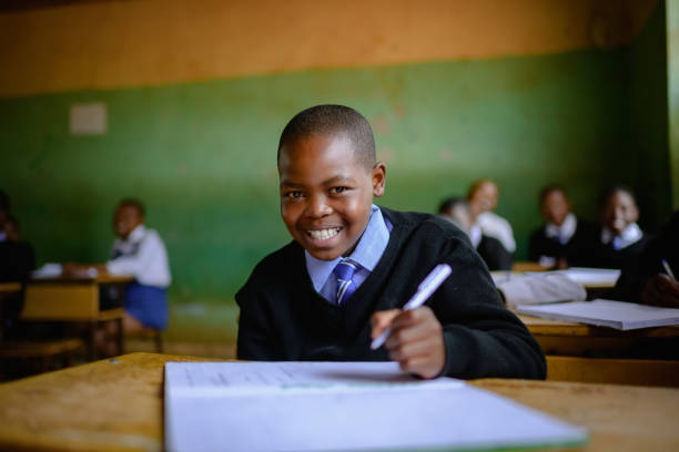 Close-up Cute Schoolboy in uniform sitting in classroom looking at camera smiling