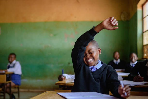 istock Cute Shy Schoolboy in uniform sitting in classroom hand raised smiling 2150086782