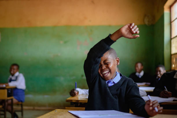 istock Cute Shy Schoolboy in uniform sitting in classroom hand raised laughing 2150086818