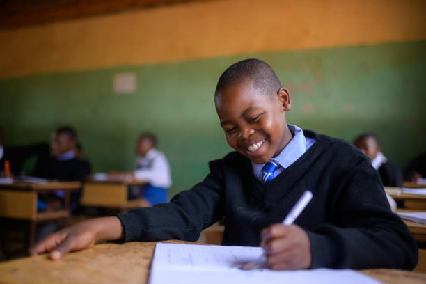 istock Cute Schoolboy in uniform sitting in classroom looking at his handwriting smiling 2150087048