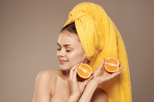 Pretty woman bared shoulders oranges in the hands of a yellow towel on her head. High quality photo