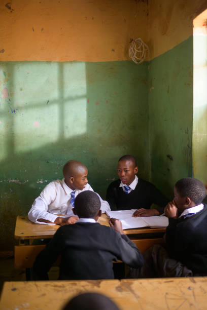Teamwork.  Brainstorming.  Discussion.  Leadership.  Group of African teenagers discussing working in a group in a school classroom.  They are wearing school uniform.  There is a feeling of togetherness and a positive emotion.  Light is streaming in from the window showing light against the green wall behind the students.   It feels like the morning session.  The children are keen to learn and be educated.  Malealea Lesotho